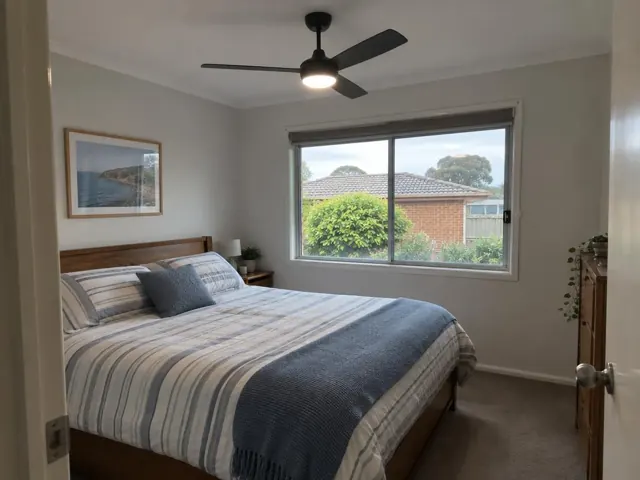 Bedroom ceiling fan over a bed in a light-coloured room with a large window in Morisset