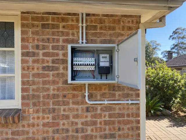 Open outdoor switchboard with meter and breakers on a brick exterior wall in Cooranbong